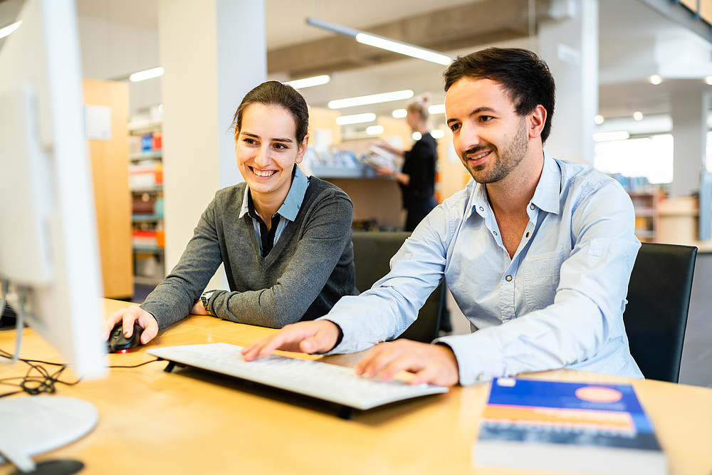 Zwei Studierende (männilich und weiblich) sitzen vor einem Computerbildschirm