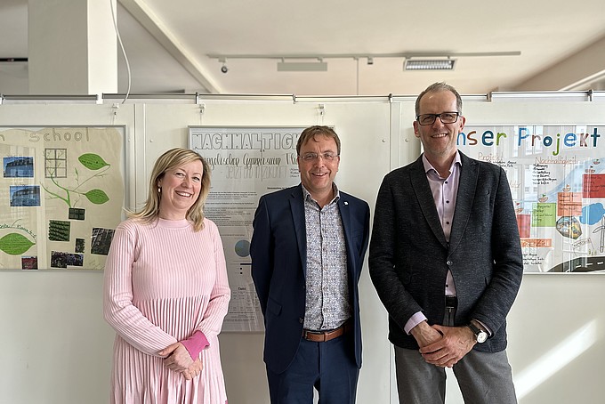 A group photo: the Vice-Rector, the Dean and the Chair of the Friends' Association in front of a poster wall on the topic of sustainability.
