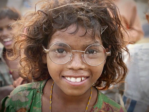 Indisches Mädchen trägt eine Brille und lächelt in die Kamera.