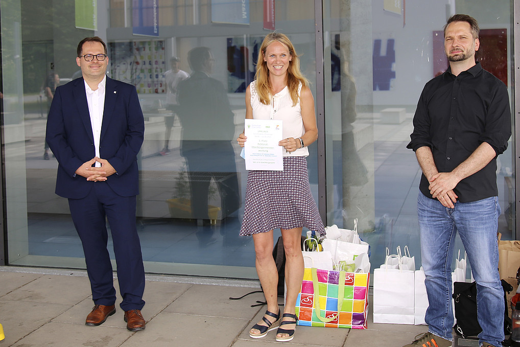 Rector Alexander Kratzsch, Jenny König and Sebastian Riedel smile at the camera and show off their pedometer challenge victory certificate for the Rectorate.