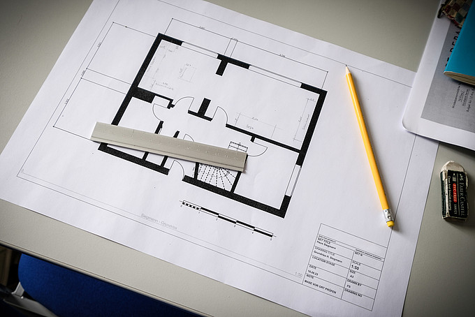 A floor plan of an apartment lies on a seminar table. On it is a yellow pencil and a ruler.