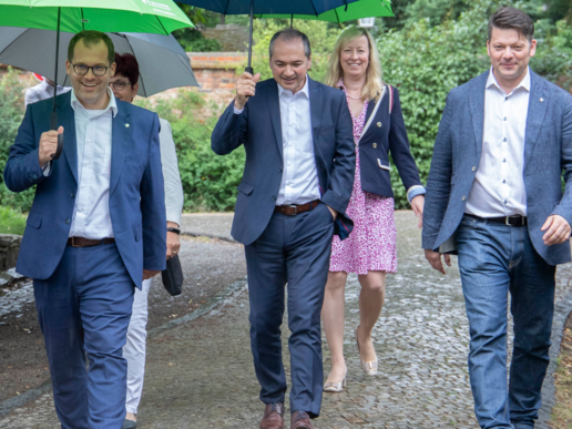 Rector Alexander Kratzsch, Görlitz Mayor Octavian Ursu, Zittau Mayor Thomas Zenker (front, from left to right) as well as Chancellor Karin Hollstein and Vice-Rector Sophia Keil. The weather is rainy, the footpath is wet. Apart from Mayor Zenker, everyone is carrying an umbrella.