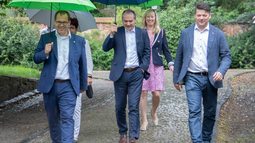 Rektor Alexander Kratzsch, Görlitz OB Octavian Ursu, Zittaus OB Thomas Zenker (vorn, von links nach rechts) sowie Kanzlerin Karin Hollstein und Prorektorin Sophia Keil. Das Wetter ist verregnet, der Fußweg ist naß. Außer OB Zenker tragen alle einen Schirm.  