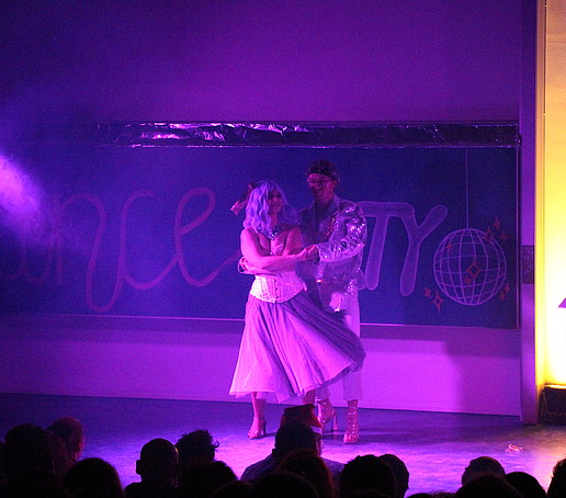 A dancing couple dances on stage in the purple light.