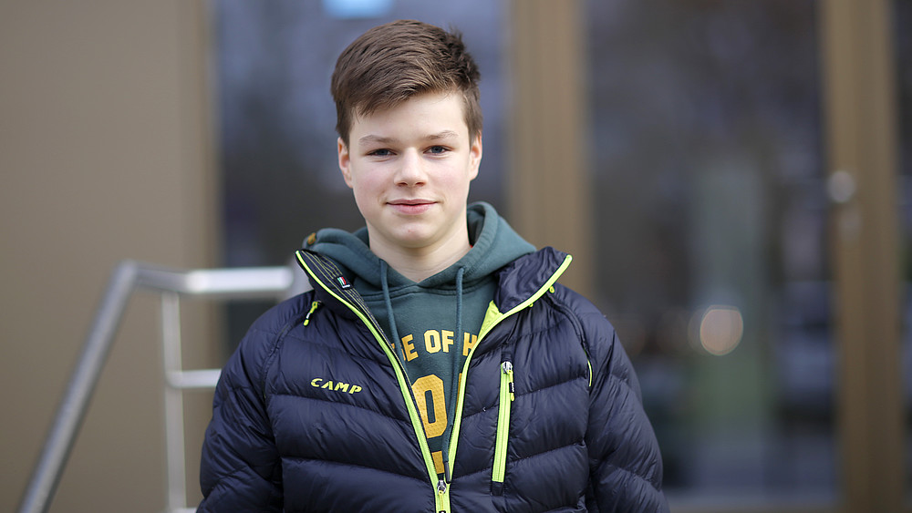 Justus stands in front of building Z 1 and smiles at the camera.