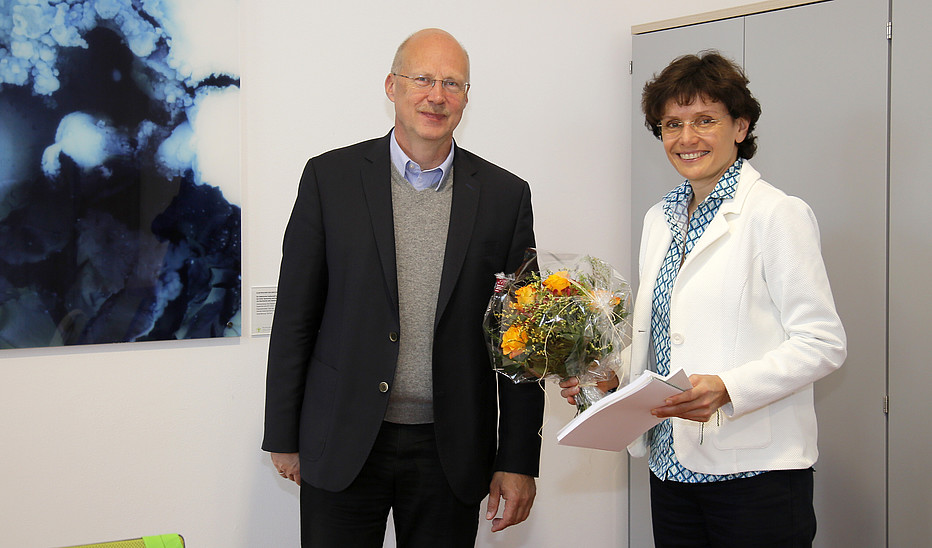 Foto: Jens Freudenberg Der Vorsitzende des Hochschulrates und das neue Mitglied Katrin Bartsch stehen im Senatssaal und lächeln in die Kamera. Frau Bartsch hält einen Blumenstrauß in der Hand.