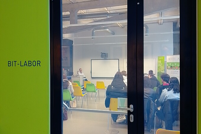Through a closed glass door you can see rows of chairs from behind, where pupils are sitting.