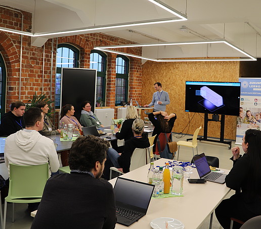 Workshop participants sit at a table and listen to a speaker.
