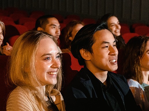 Young people sit in the movie theater and laugh while watching the screen.