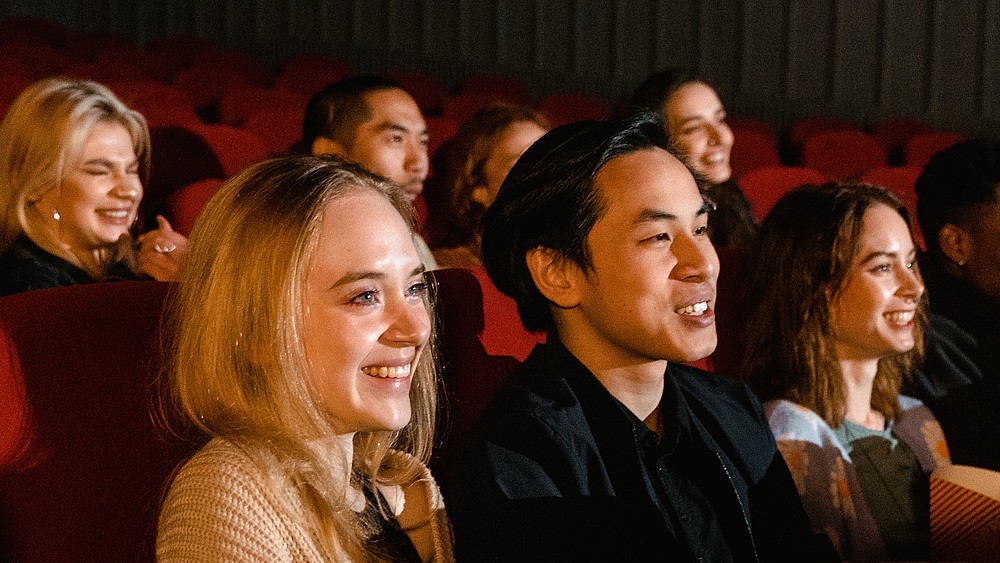 Young people sit in the movie theater and laugh while watching the screen.