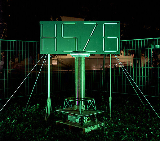 The HSZG logo is illuminated in neon green by fluorescent tubes.