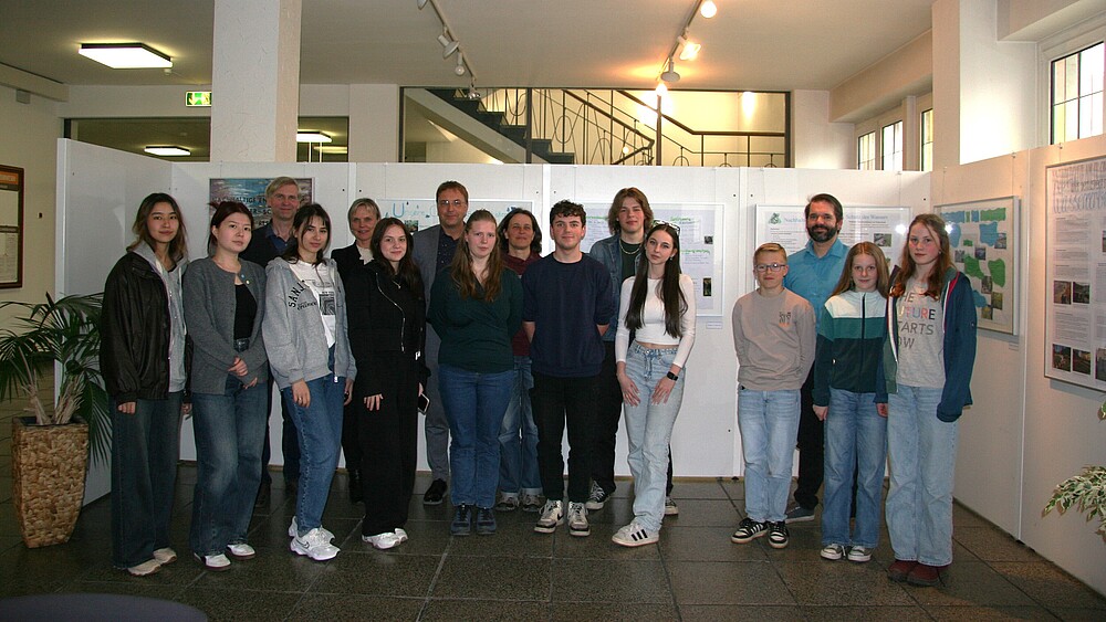Pupils, teachers and Prof. Kroschel stand next to each other in front of a picture exhibition.