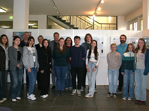 Pupils, teachers and Prof. Kroschel stand next to each other in front of a picture exhibition.