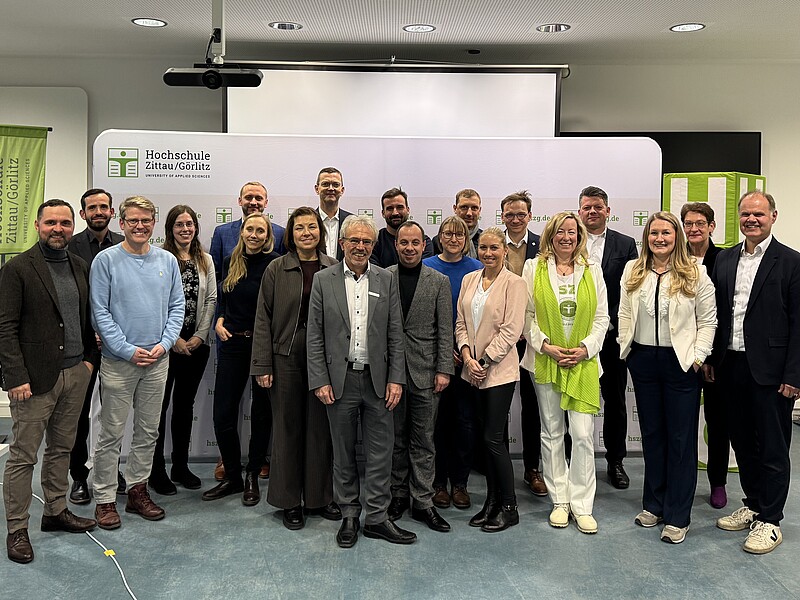 Mehrere Menschen stehen als Gruppe vor einer weißen Pressewand und lächeln in die Kamera.