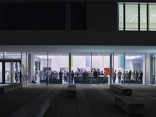 Haus vier von außen, durch die Glasfassade sieht man die Gäste der Veranstaltung miteinander im Gespräch.