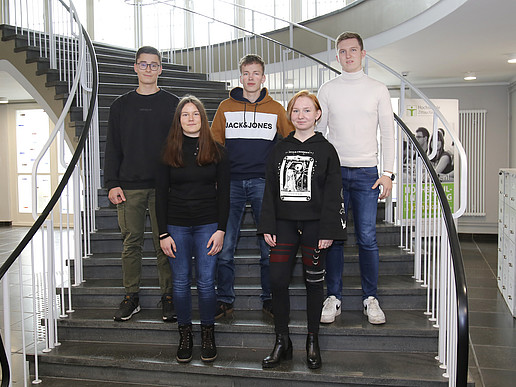 The trainees stand in two rows on the stairs and smile at the camera.