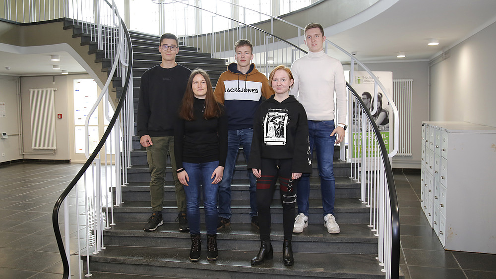 The trainees stand in two rows on the stairs and smile at the camera.