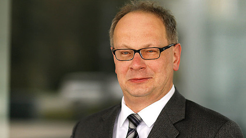 Prof. Meißner trägt Brille und Anzug mit Krawatte. Er lächelt in die Kamera.