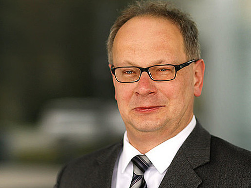 Prof. Meißner trägt Brille und Anzug mit Krawatte. Er lächelt in die Kamera.
