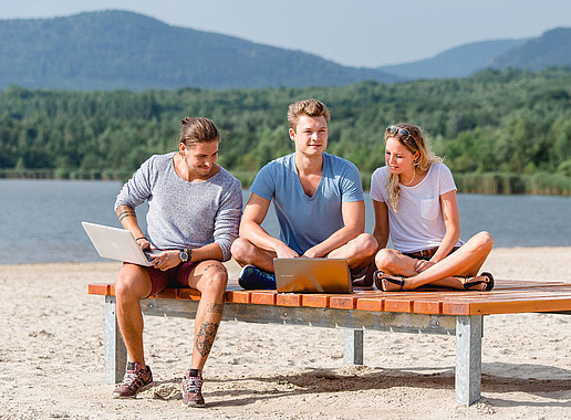 Zwei Studenten und eine Studentin am Olbersdorfer See auf einer Bank am Strand.