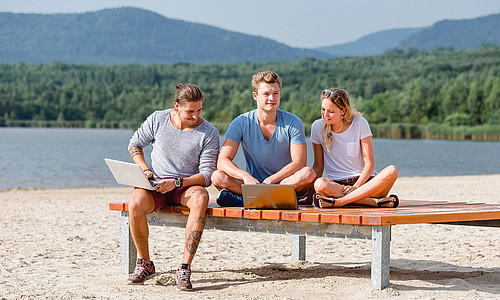 Zwei Studenten und eine Studentin am Olbersdorfer See auf einer Bank am Strand.