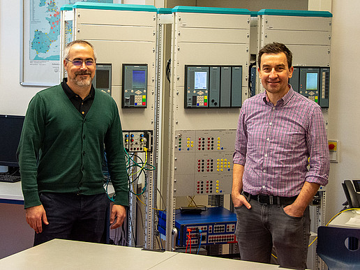 Federico Canas (links) und Prof. Cezary Dzienis (rechts) bei der Inbetriebnahme der digitalen Schnittstelle mit nichtkonventionellen Wandlern. Im Hintergrund befinden sich weitere Versuchsstände mit digitalen Schutzgeräten (SIPROTEC 5, Siemens AG).