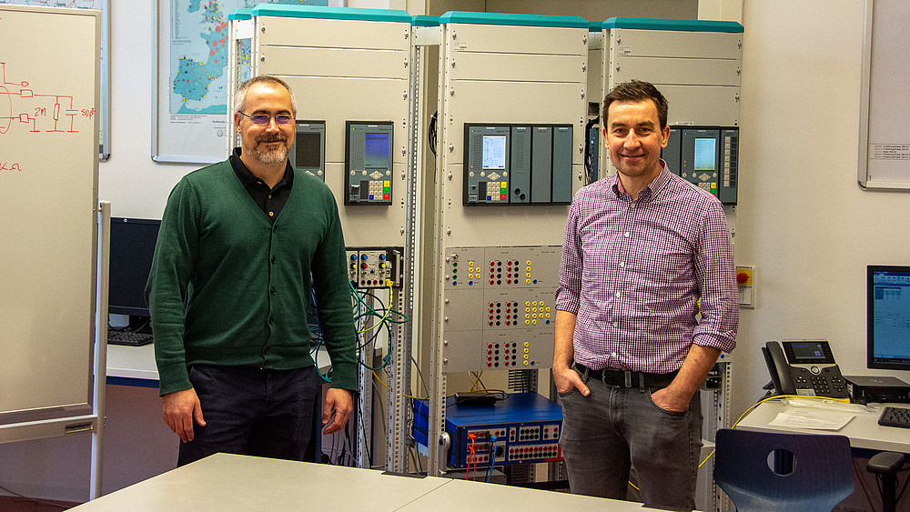 Federico Canas (links) und Prof. Cezary Dzienis (rechts) bei der Inbetriebnahme der digitalen Schnittstelle mit nichtkonventionellen Wandlern. Im Hintergrund befinden sich weitere Versuchsstände mit digitalen Schutzgeräten (SIPROTEC 5, Siemens AG).