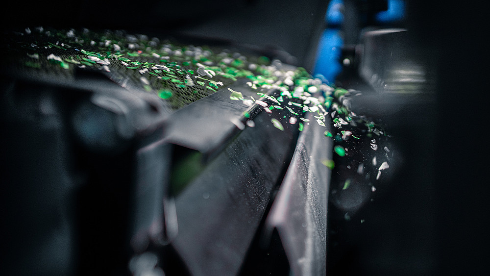Green plastic flakes fly out of a machine.