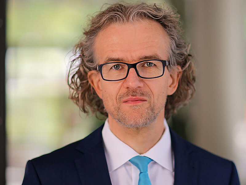 Prof. Saatkamp wears glasses and a light blue tie and looks into the camera.