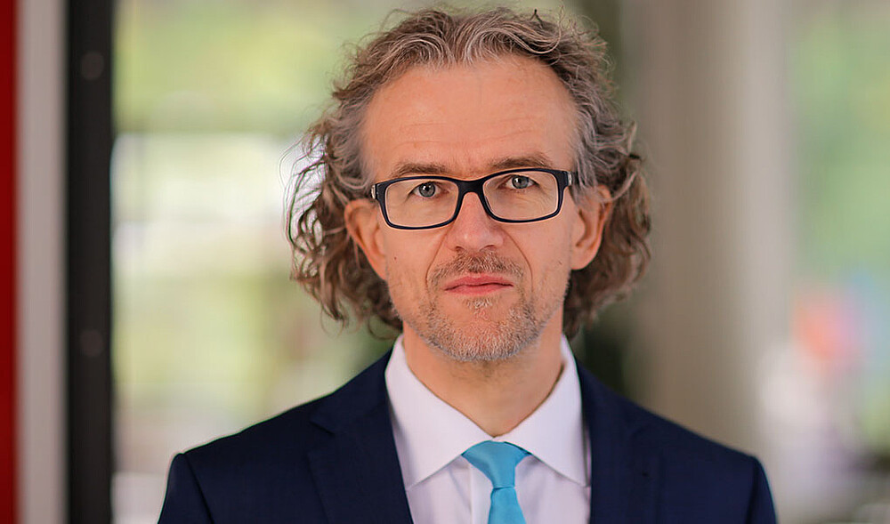 Prof. Saatkamp wears glasses and a light blue tie and looks into the camera.
