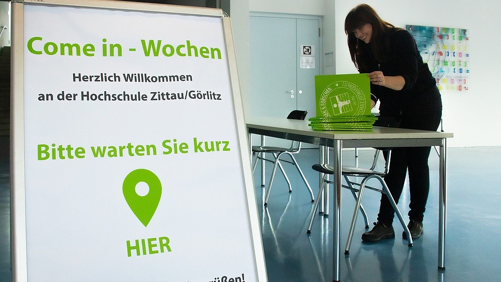 A display with the words Come-In Weeks in the foyer of House Z four. In the background, a member of staff leafs through a folder.