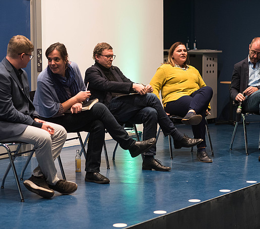 5 people sit on chairs on a stage.
