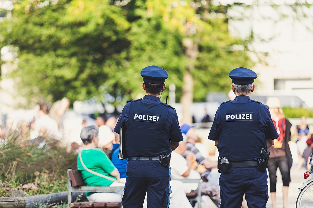 Two police officers stand in a park with their backs to the camera, facing forward.