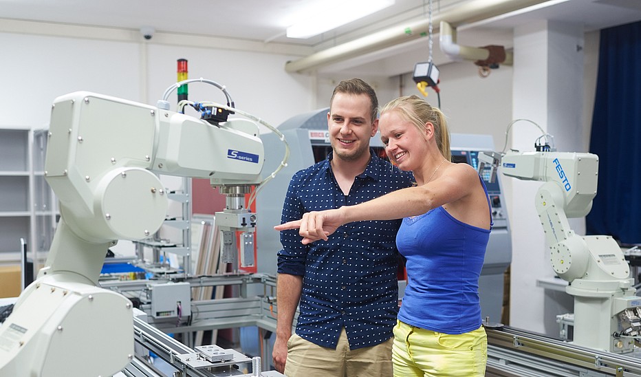 Foto: HSZG Zwei junge KIA-Studierende stehen im Robotik-Labor und schauen sich die Technik an.