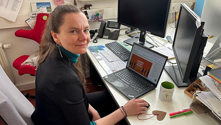 Julia Ochmann sitzt am Schreibtisch vor einem aufgeklappten Laptop und schaut in die Kamera.