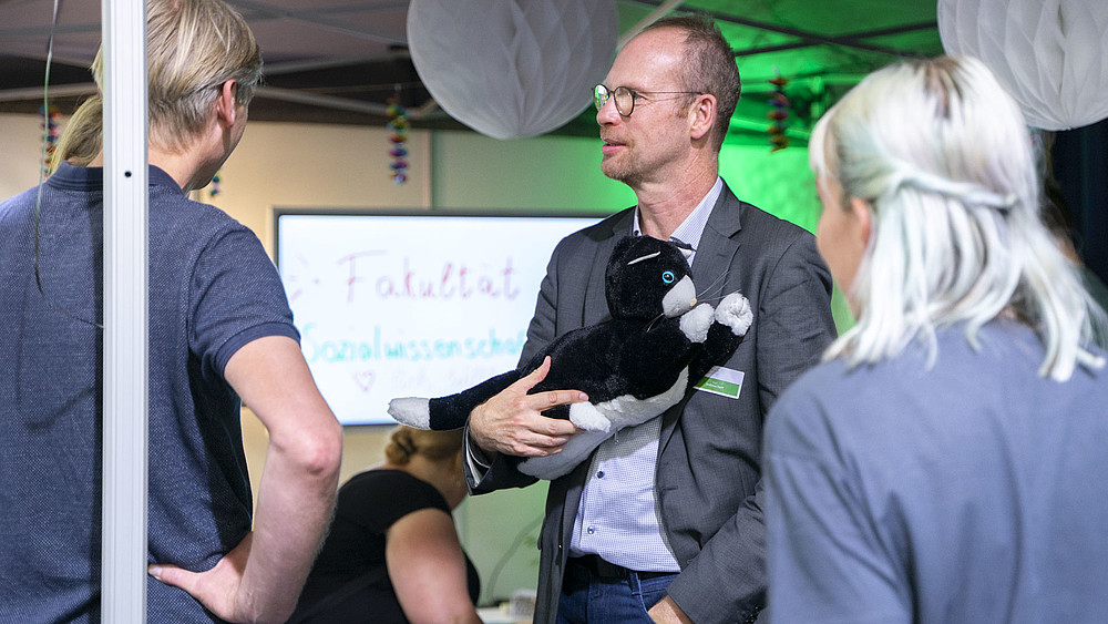 GAT Institute Director Prof. Andreas Hoff holds the JustoCat at the trade fair stand at the INSIDERTREFF in Löbau.