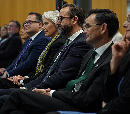 Several people sit in a row and listen attentively to an event.