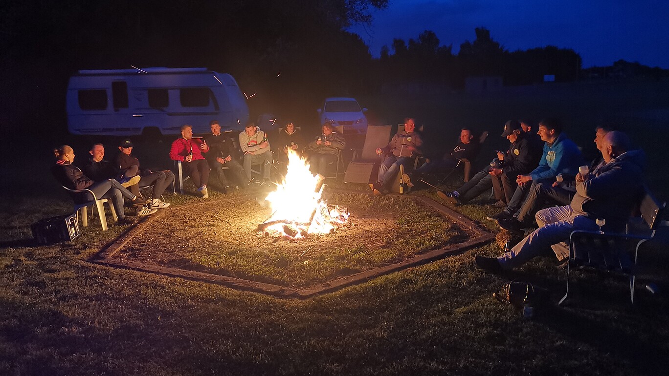 Students sit around a campfire in a field.