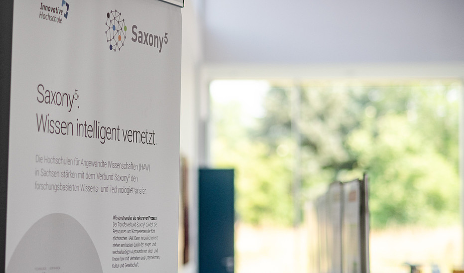 Foto: HSZG Ein Rollup von Saxony5 steht in einer Halle, aus der der Blick ins Grüne fällt.