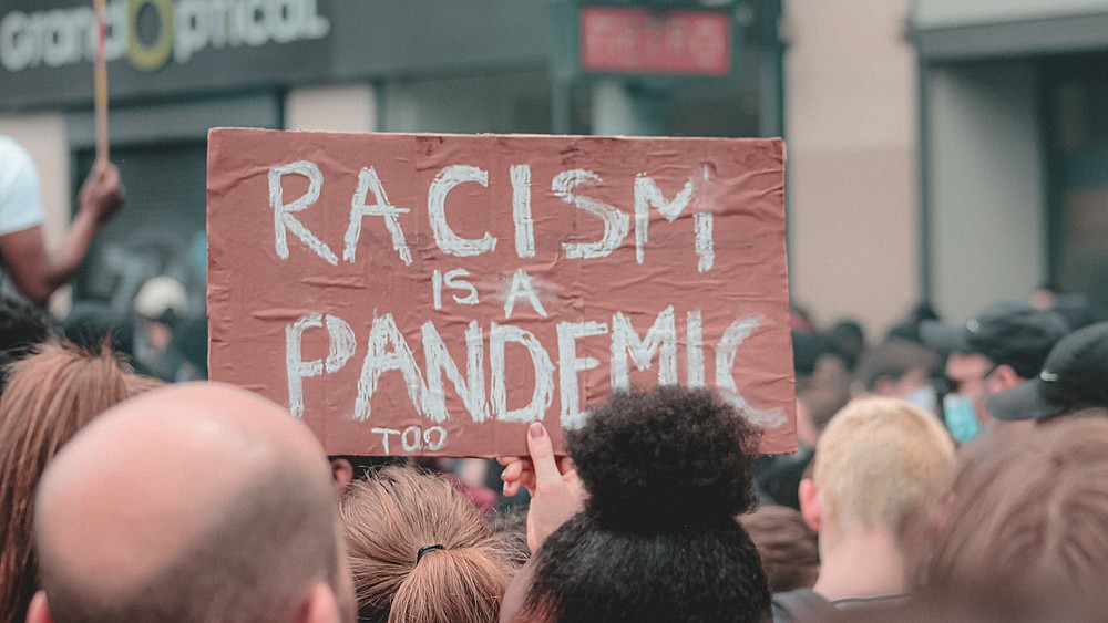 Demonstrierende gegen Alltagsrassismus halten ein Schild mit der Aufschrift "Rassismus ist auch eine Pandemie" in die Höhe.