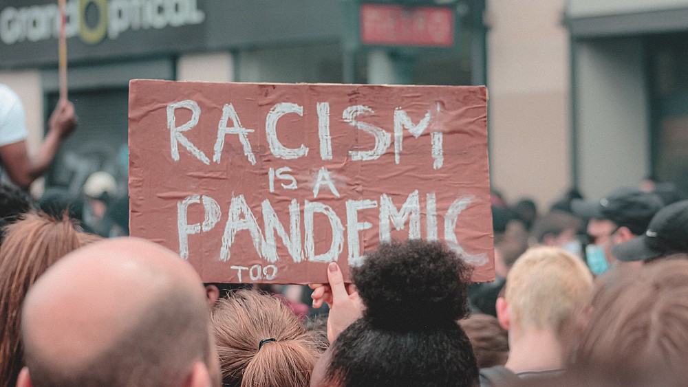 Demonstrators against everyday racism hold up a sign reading "Racism is also a pandemic".