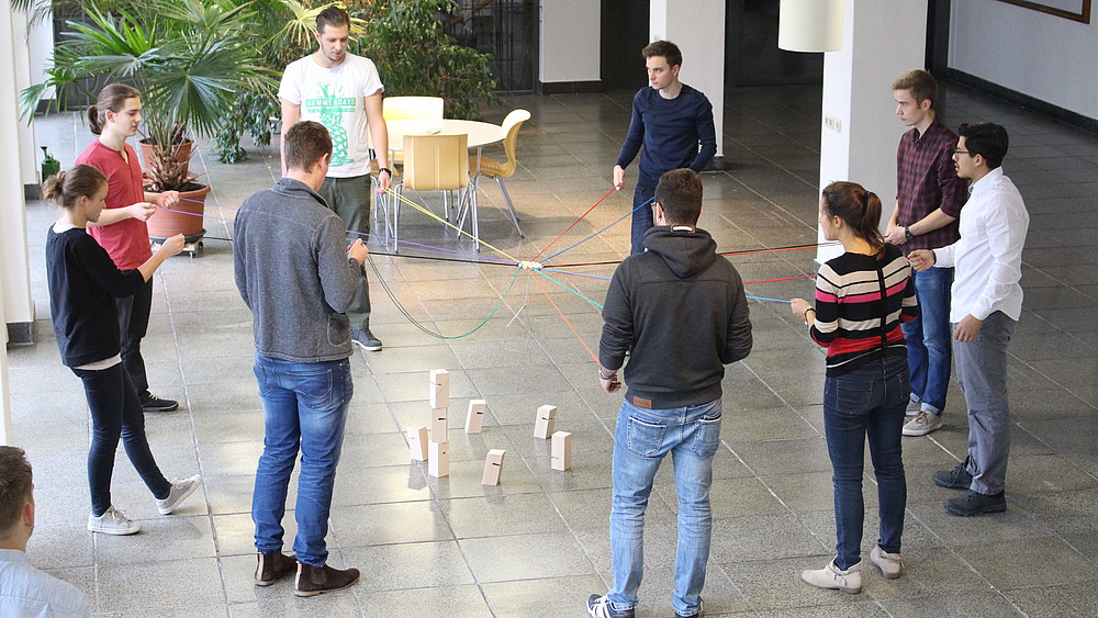 Studierende stehen im Kreis und halten Fäden in der Hand.