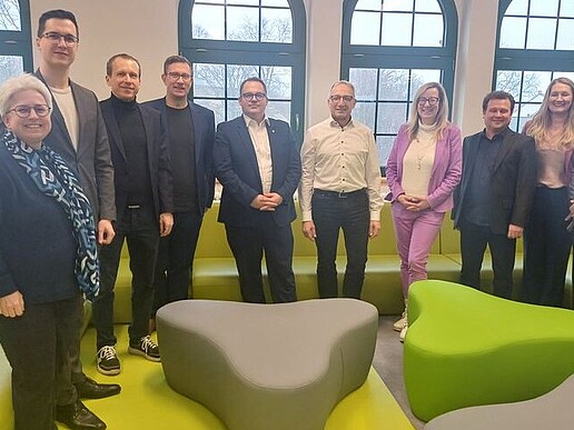 Representatives of the HSZG and Fraunhofer ENAS stand between green furniture for a group photo and smile into the camera.
