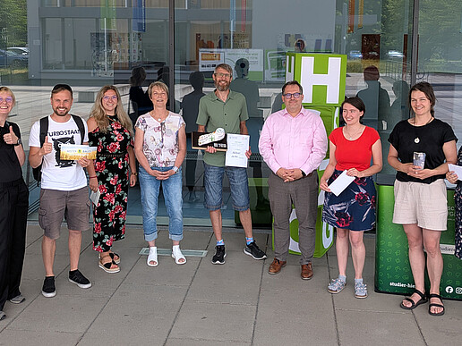 The rector, representatives from the university's health management team and participants stand next to each other in front of building four for a group photo.
