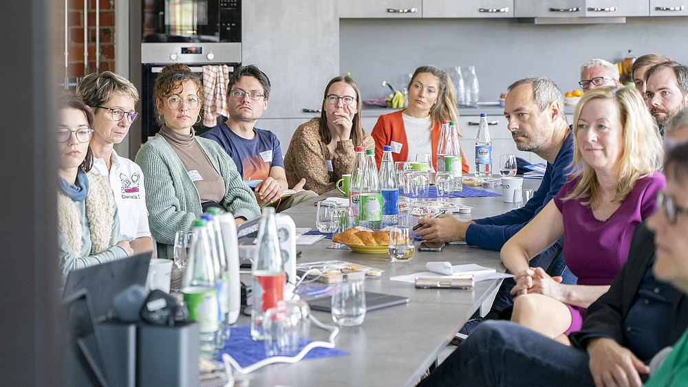 University employees and guests sit at a long table in Celsiuz and listen to a lecture.