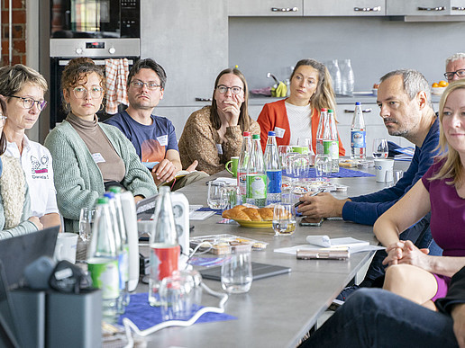University employees and guests sit at a long table in Celsiuz and listen to a lecture.