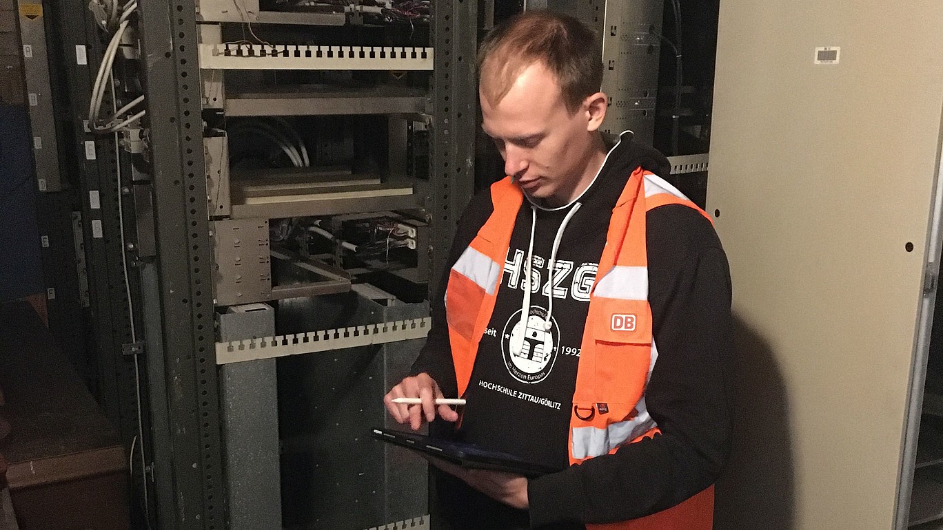 A man stands at a control cabinet with a stylus and looks at a tablet