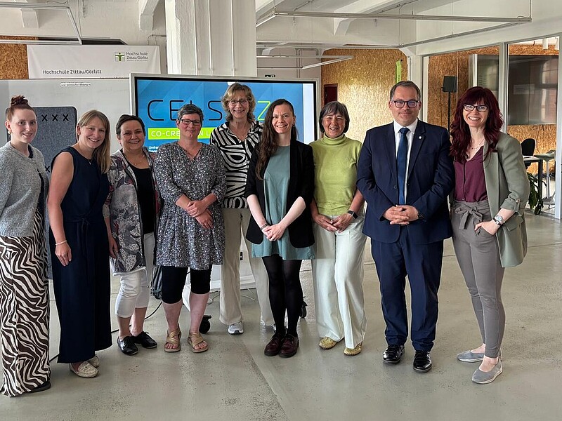 Die Mitarbeiterinnen im Professorinnenprogramm stehen mit dem Rektor im Celsiuz zum Gruppenfoto in einer Reihe und lächeln in die Kamera.