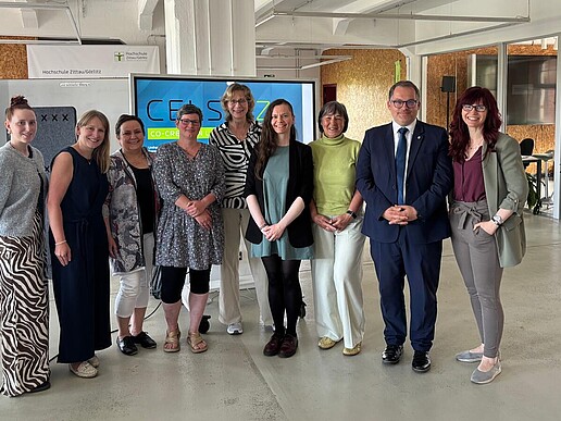 The women participating in the Women Professors Program stand in a row with the president at Celsiuz for a group photo and smile at the camera.