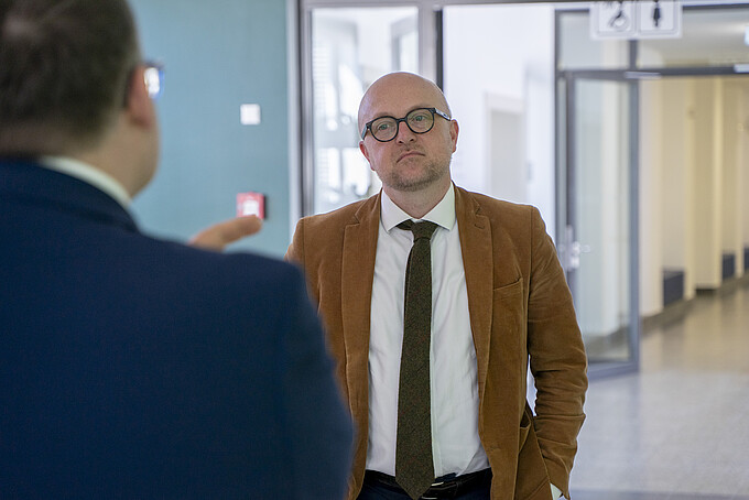 Mr. Denk stands in the hallway of house one and listens to the principal standing in front of him.